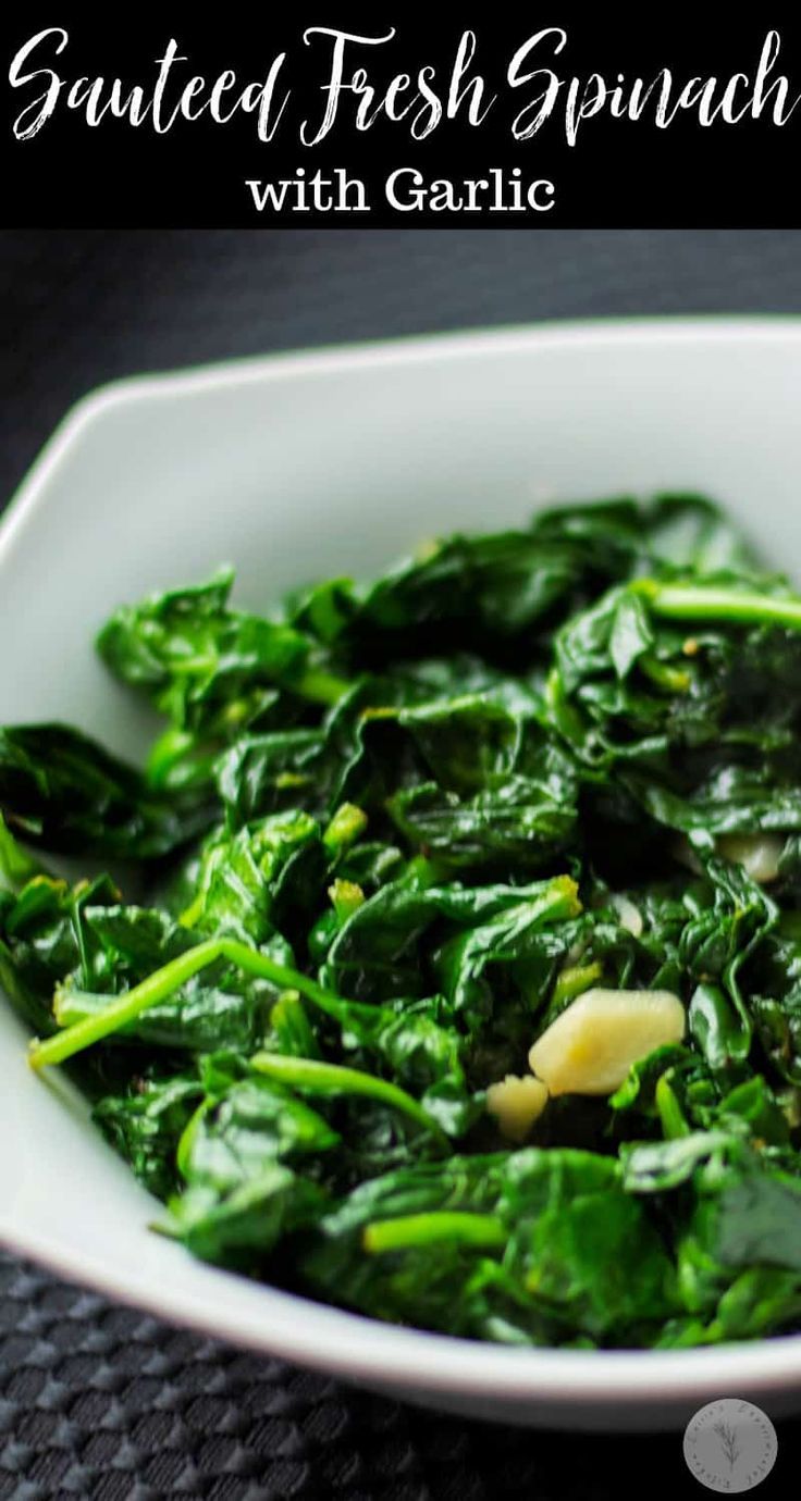 a white bowl filled with spinach on top of a black table next to a spoon