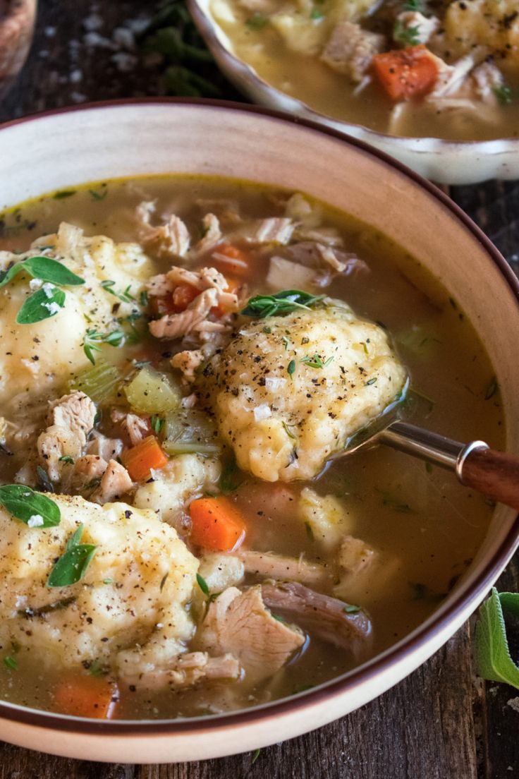 two bowls filled with chicken and dumplings on top of a wooden table next to bread