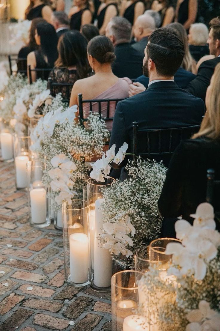 a row of chairs filled with white flowers and candles sitting on top of a brick floor