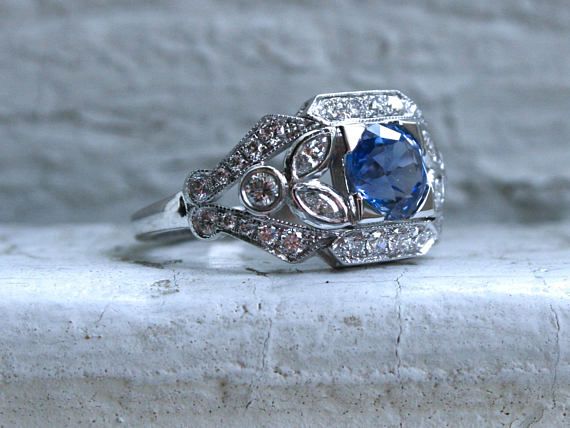 a blue and white diamond ring sitting on top of a stone slab with diamonds around it