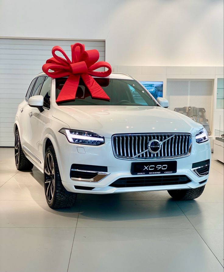 a white volvo car with a large red bow on the hood, parked in a showroom