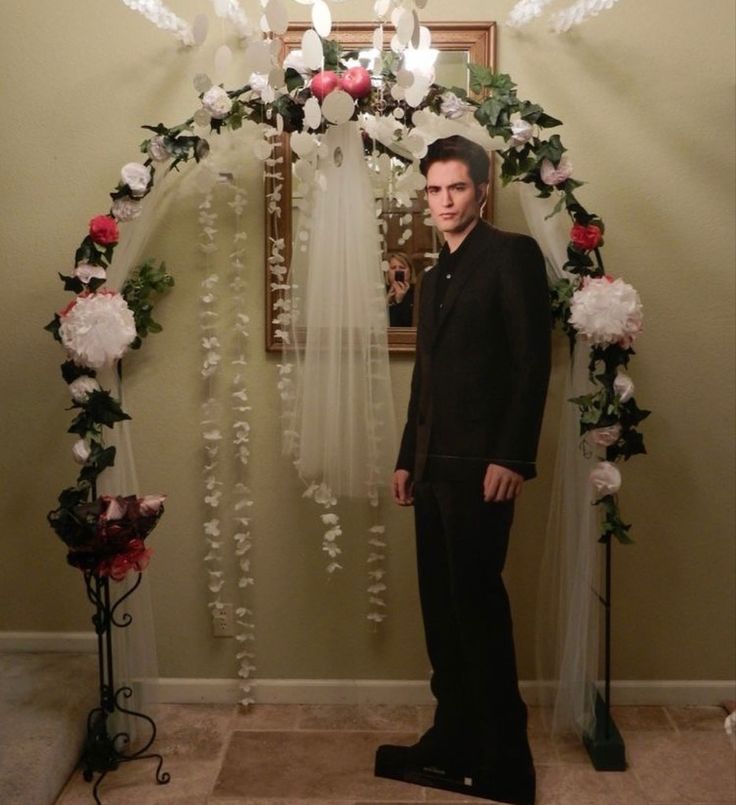 a man standing in front of a wedding arch decorated with white and pink flowers on it