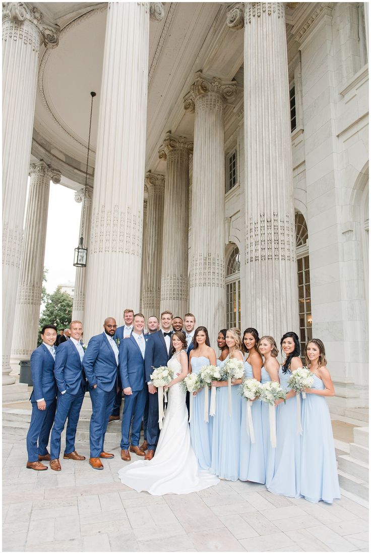 a large group of people standing in front of a building with columns and flowers on the ground