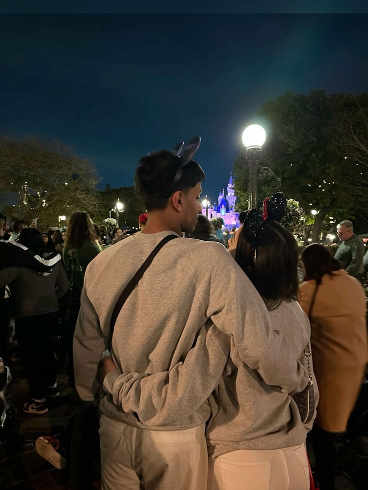 a man and woman standing in front of a castle at night with their back to the camera