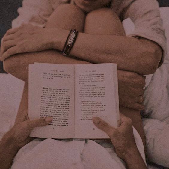 a person laying in bed reading a book with their hands on top of the book