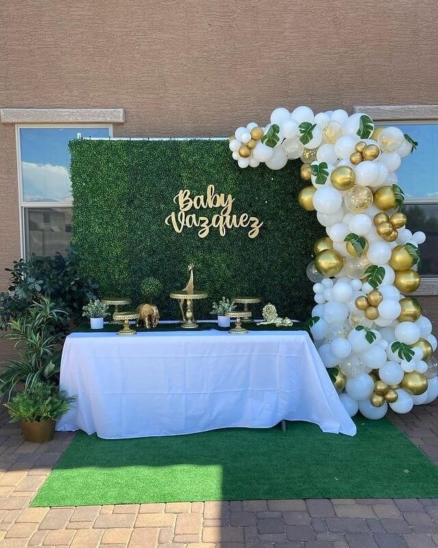 a baby shower is set up outside with balloons and greenery on the side of the wall