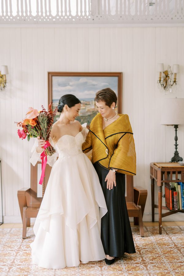 two women standing next to each other in front of a painting and holding bouquets