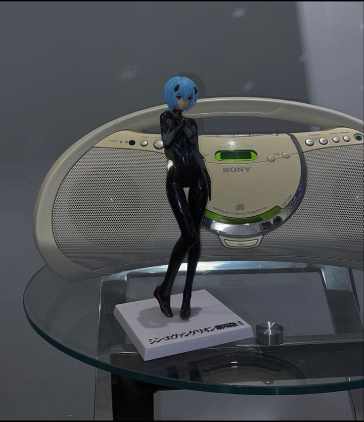 a figurine stands on top of a glass table with a radio in the background