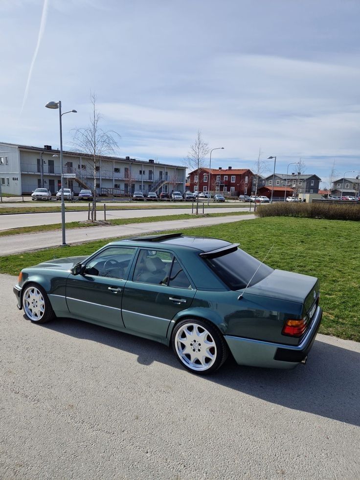 a green car parked on the side of a road next to a grass covered field