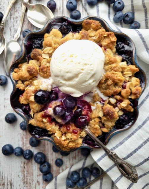 a blueberry cobbler with ice cream on top and spoons next to it