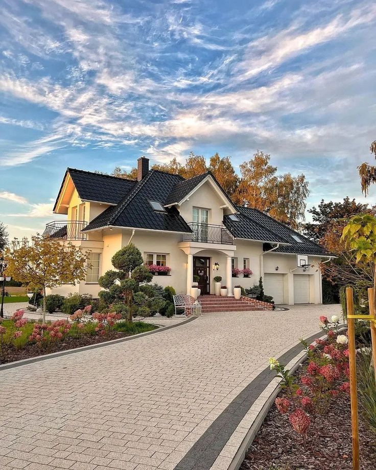 a large house that is in the middle of some flowers and plants on the sidewalk