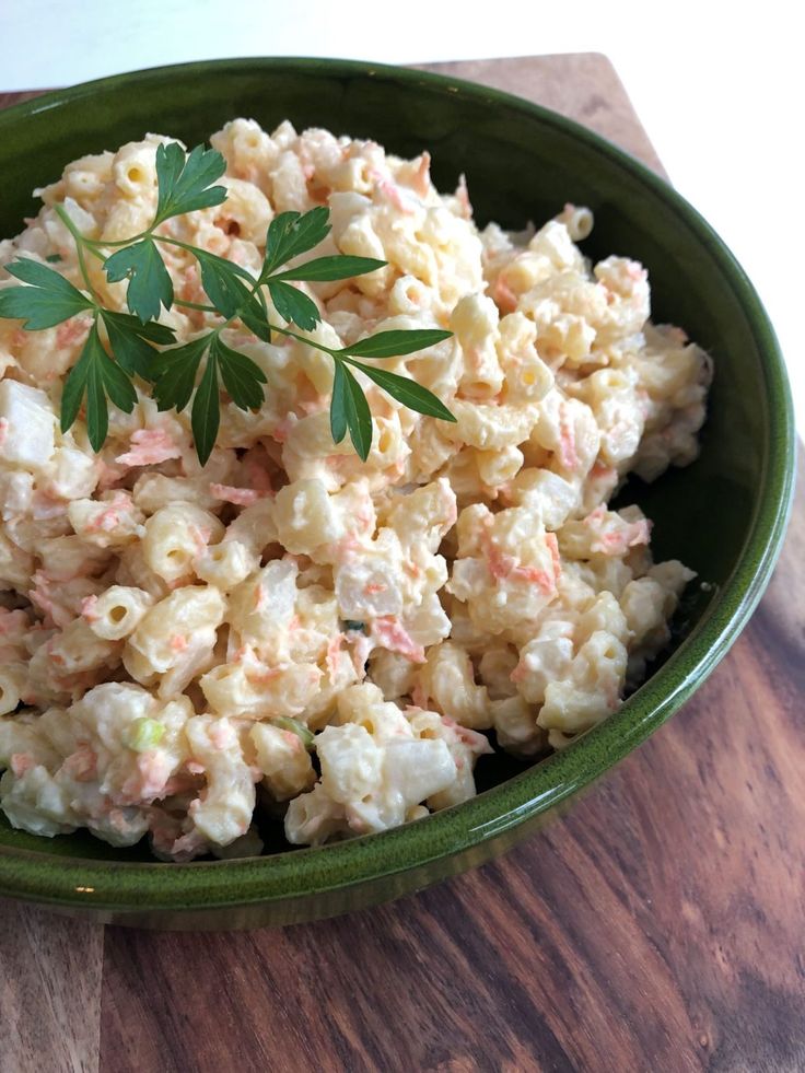 a green bowl filled with macaroni salad on top of a wooden table