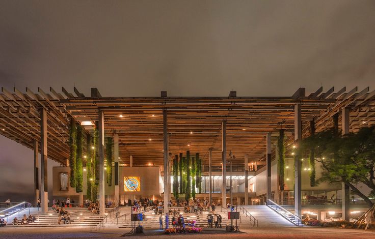 a large building with people walking around it and lights on the side of the building