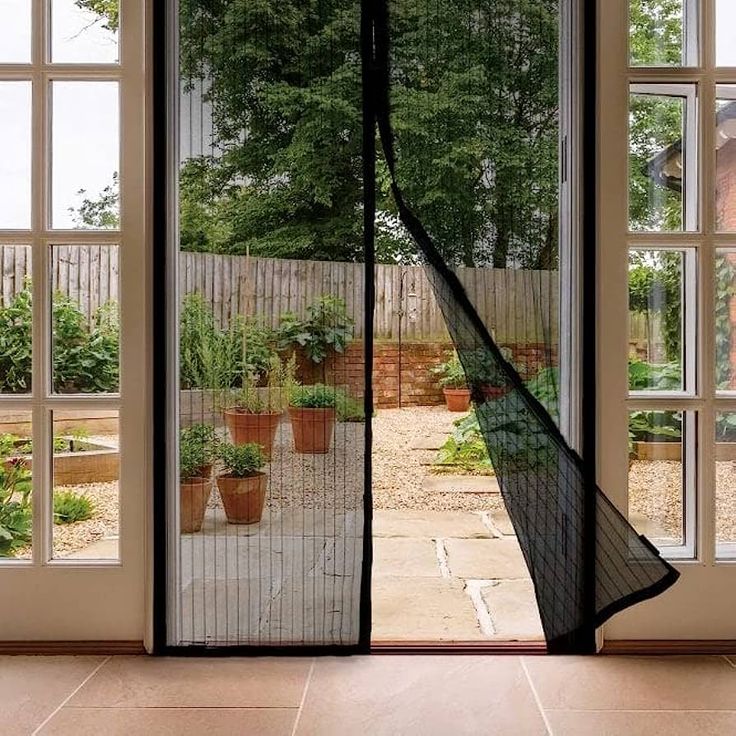 an open patio door with sheer curtains on the side and potted plants behind it