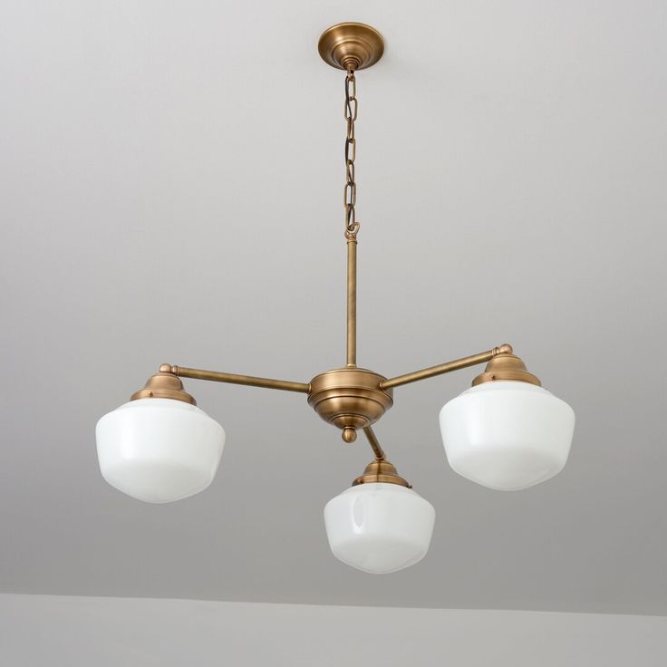 three white glass shades hang from an antique brass chandelier