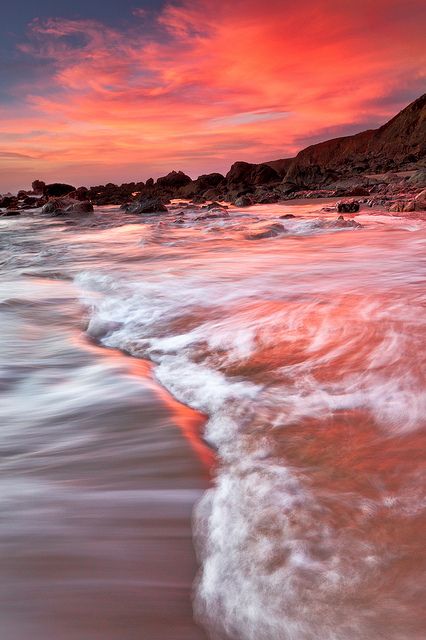 an ocean beach with waves coming in to shore and the sun setting over the water