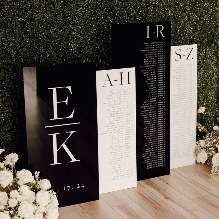 two black and white signs sitting on top of a wooden floor next to some flowers