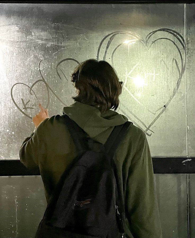 a person standing in front of a frosted glass wall with hearts drawn on it