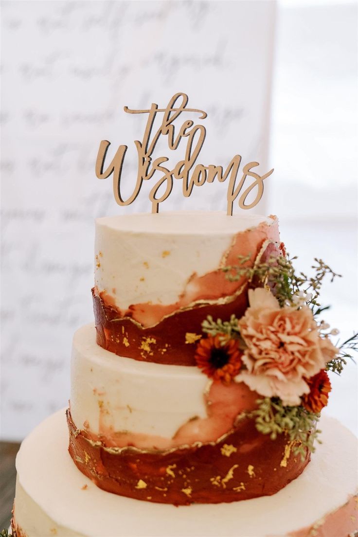 a three tiered wedding cake with flowers and the words, this is us on top