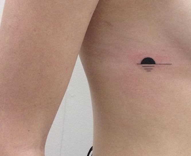 a woman's stomach with a small sun tattoo on her left side, and an arrow in the middle