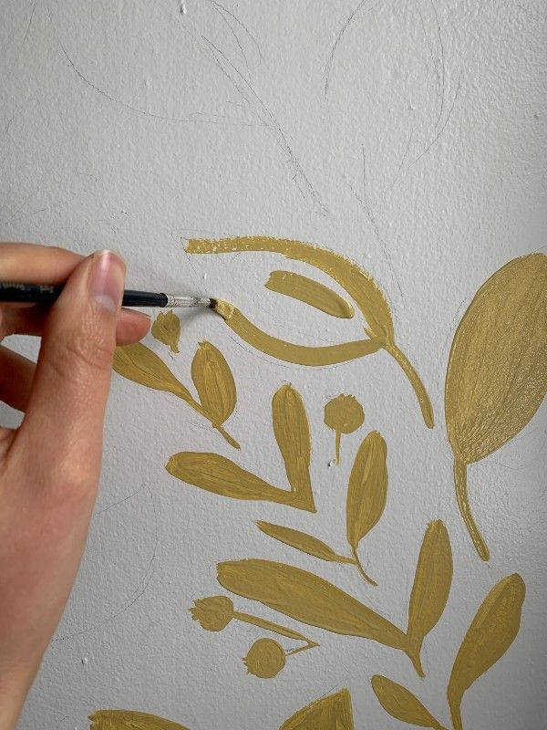 a person is using a brush to paint leaves on a white wall with gold leaf stencils