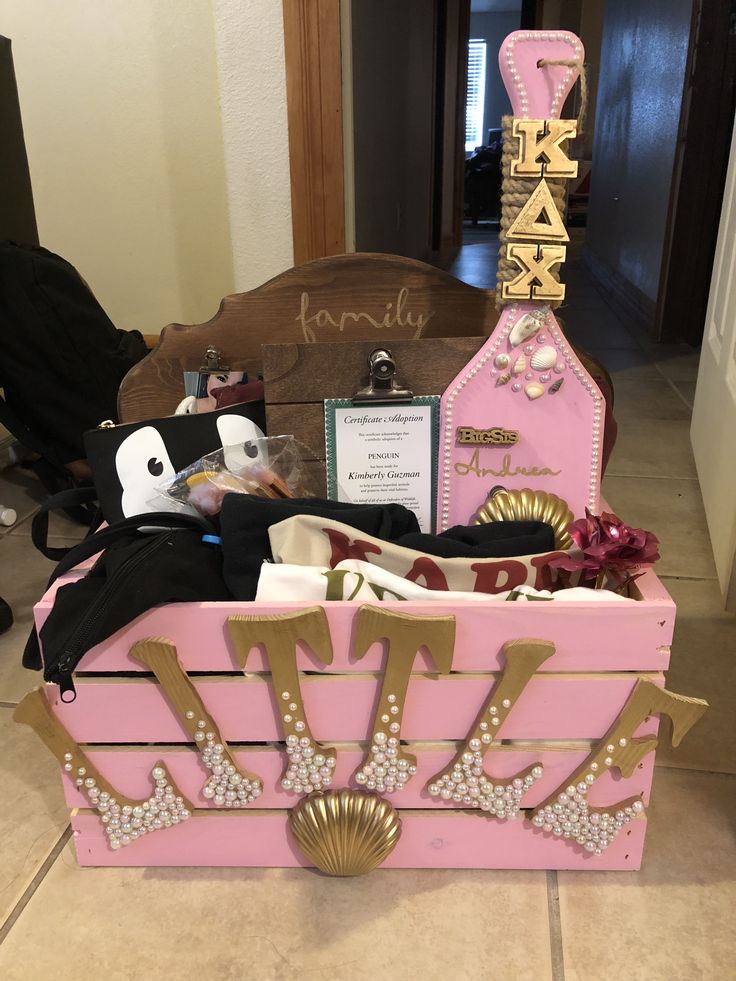 a pink trunk filled with lots of items on top of a tiled floor next to a wooden sign