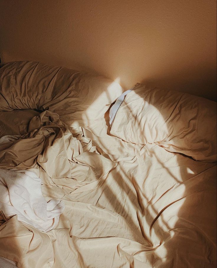 an unmade bed with the sheets pulled back and sun shining through it, in a bedroom