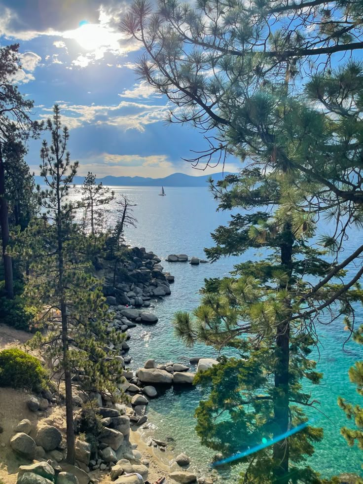 the sun shines through the clouds over the water and trees on the shore line