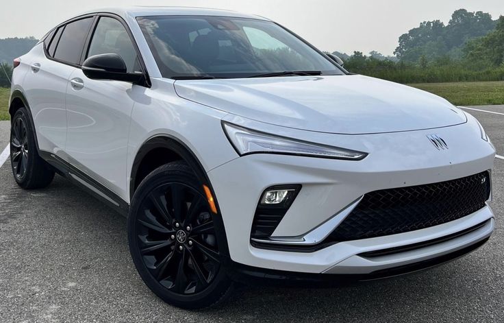 the front end of a white suv parked in a parking lot with trees and grass behind it