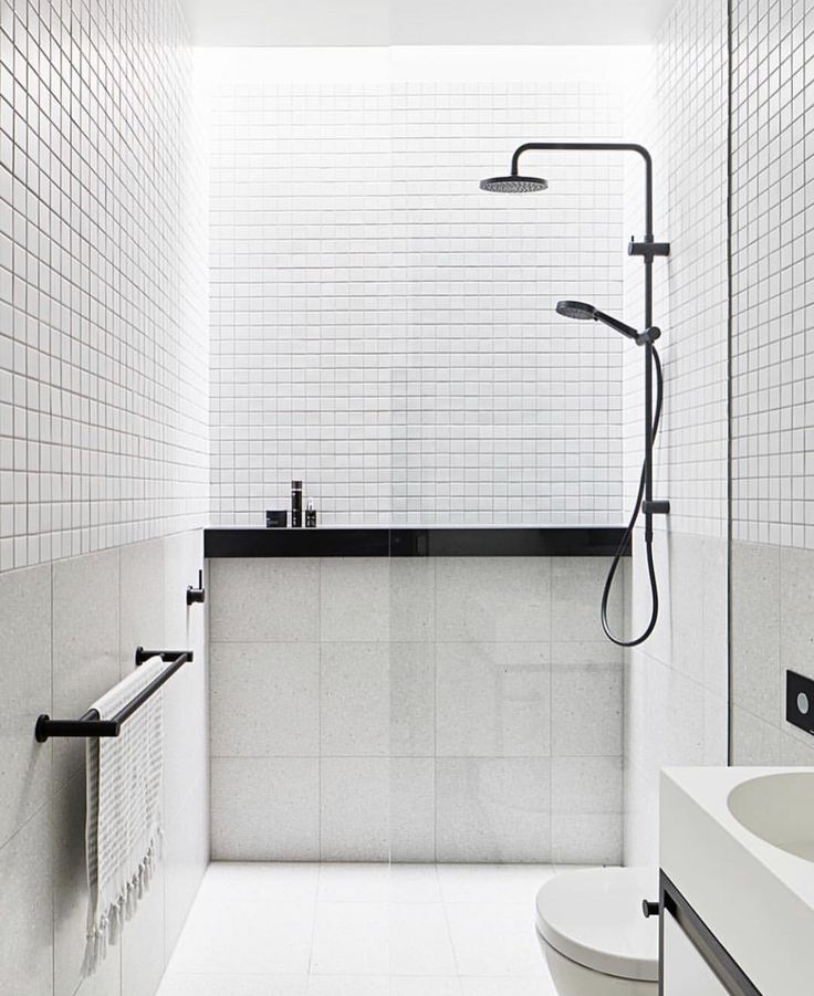 a white tiled bathroom with black accents and accessories on the shower head, sink, and toilet