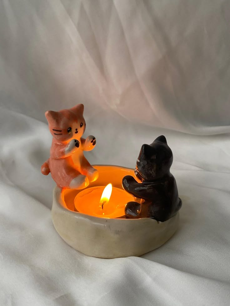 two cats sitting in a bowl with a lit candle