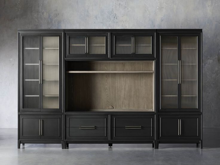 a black entertainment center with glass doors and drawers on the side, in front of a concrete wall