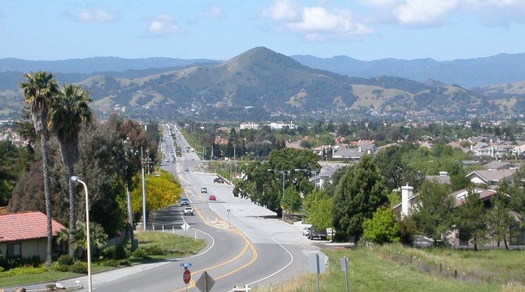 an empty street in the middle of a town with mountains in the background and houses on either side