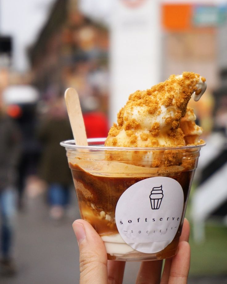 a person holding up a cup with ice cream and toppings in it on the street