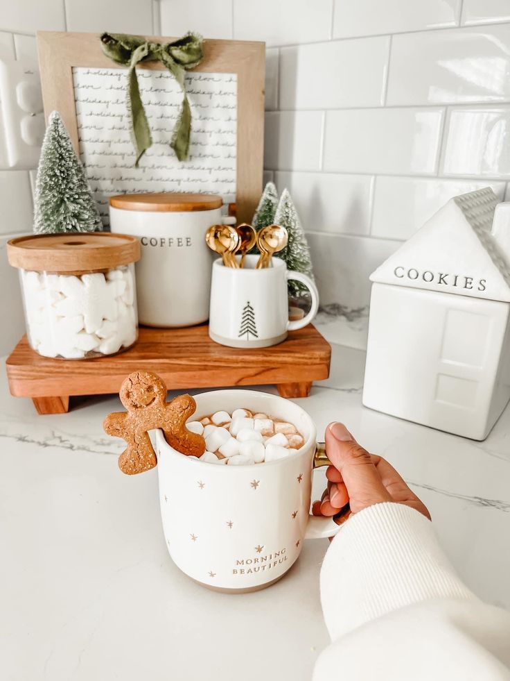 a person holding a mug with marshmallows in it on a kitchen counter