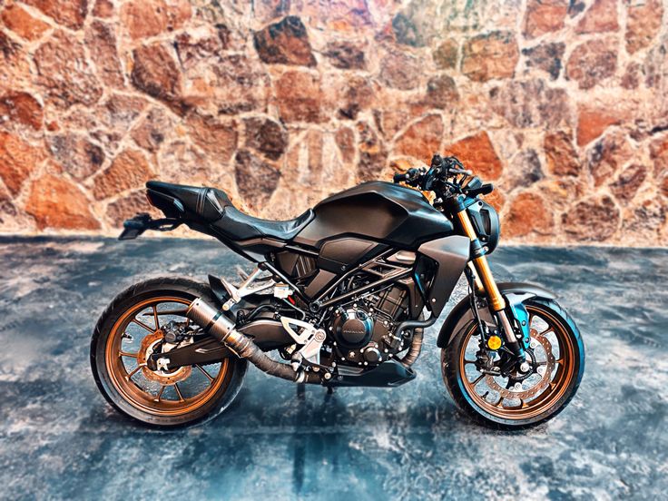 a black motorcycle parked in front of a stone wall with orange rims on it