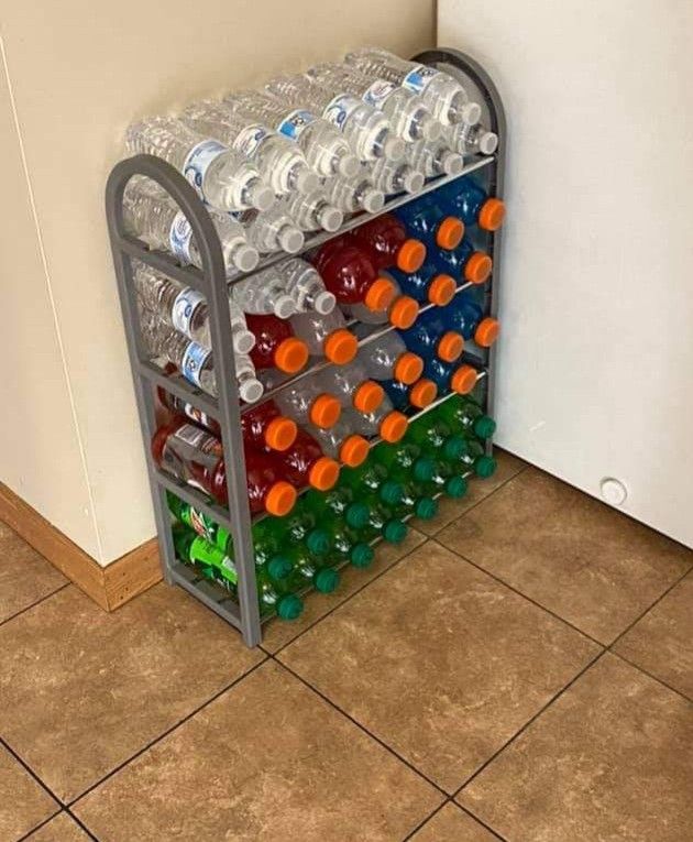 a metal rack filled with lots of water bottles next to a white wall and tiled floor