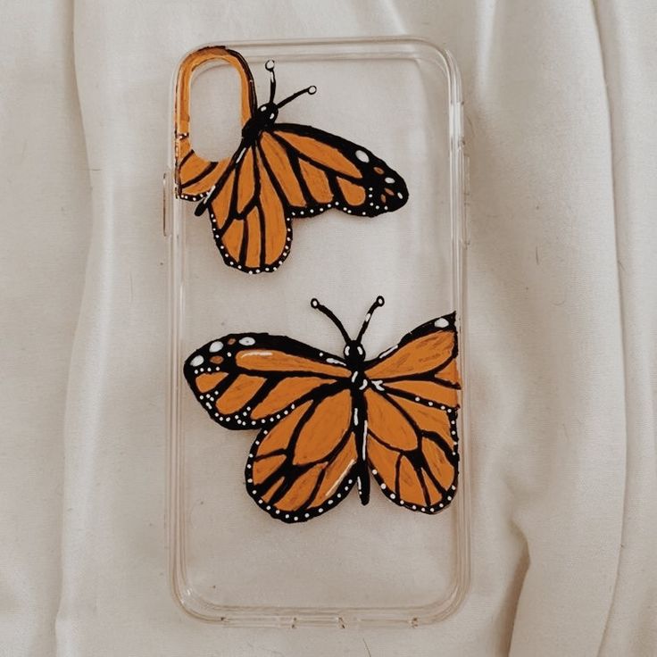 two orange and black butterflies sitting on top of a phone case next to each other