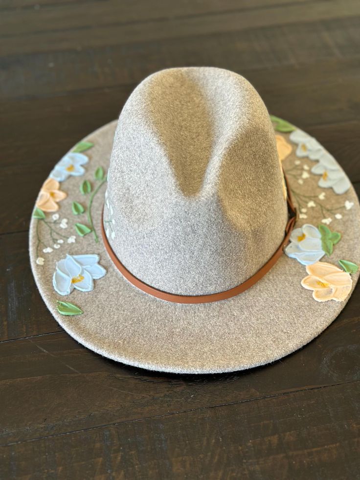 Fedora style hat with textured hand painted flowers.       -Faux leather band with gold buckle detail Material:       -65% Cotton      -35% Polyester Hat measurements:       -2.8" brim      -22.4-23.2" inner circumference      -4.7" height      -Inside circumference is fully ADJUSTABLE - there is a string pull on the inside to adjust to your perfect fit. Care Instructions:      -Spot clean only with damp cloth      -Paint can get wet and will not come off      -Do not put through the washer/drye Spring Fedora With Flat Brim, One Size, Spring Fedora With Flat Brim, One Size Fits Most, Spring Felt Hat With Curved Brim, Spring Fedora With Flat Brim, Country Style Curved Brim Hat For Spring, Cream Western Fedora For Spring, Cream Felt Hat With Flat Brim For Spring, Cream Curved Brim Felt Hat For Spring, Spring Beige Felt Hat With Curved Brim