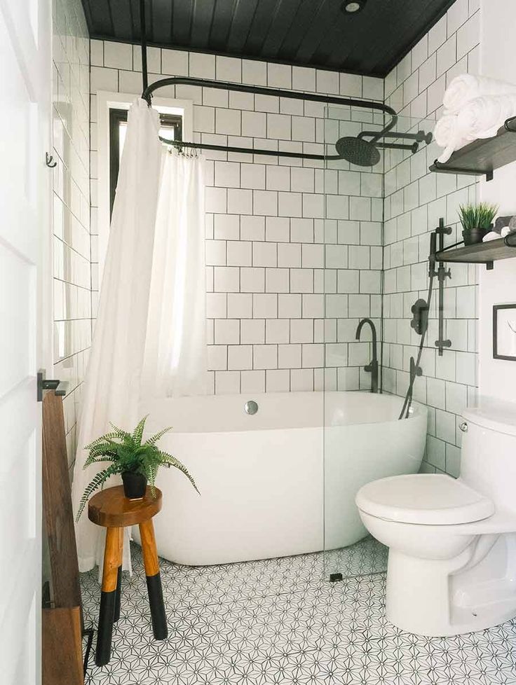 a white toilet sitting next to a bath tub under a bathroom window with black and white tiles