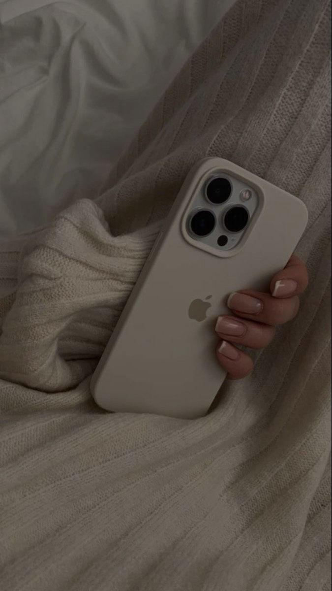 a person holding an iphone in their hand on top of a white bed covered with blankets