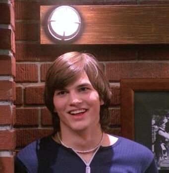 a young man standing in front of a brick wall with a clock on it's face