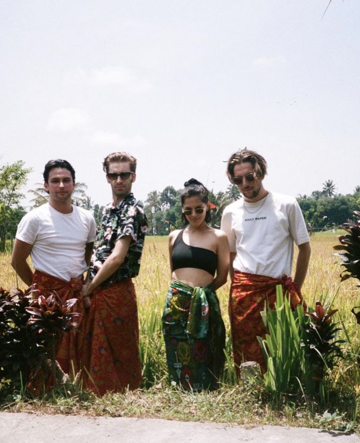 three men and two women standing in front of some tall grass with trees in the background