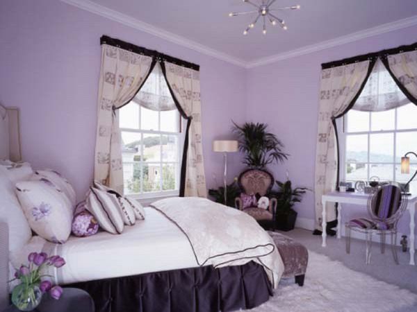 a bedroom with purple walls and white bedding, chandelier, window curtains, and chair