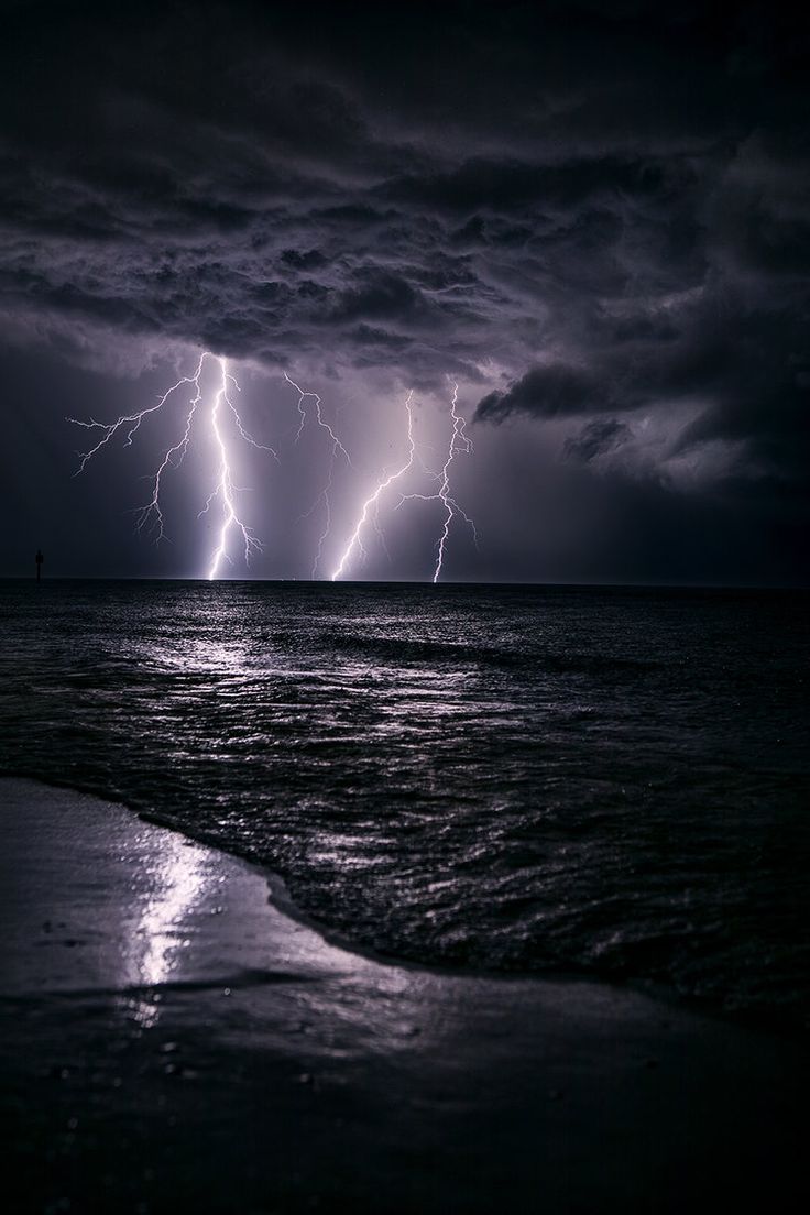 two lightning strikes over the ocean on a stormy night with dark clouds and water in the foreground