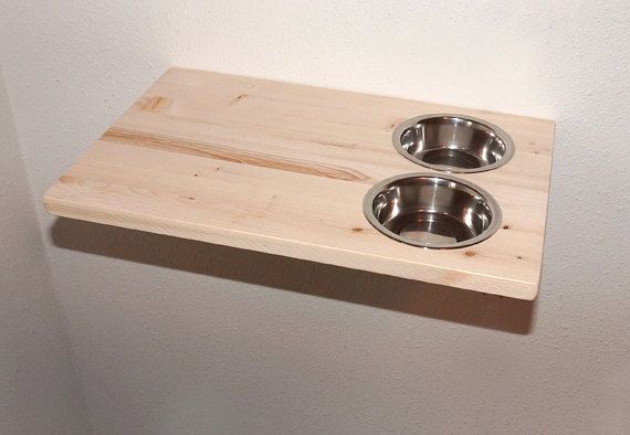 two stainless steel dog bowls on a wooden shelf in the corner of a white walled room