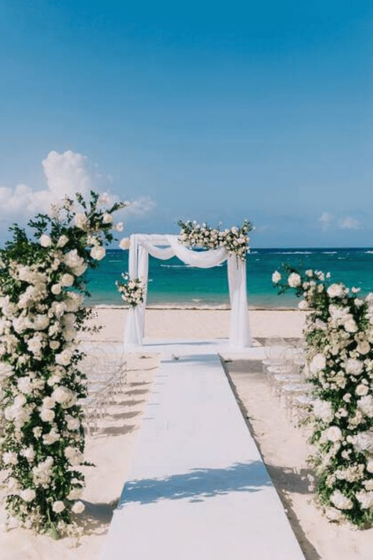 an outdoor wedding setup on the beach with white flowers and greenery at the end