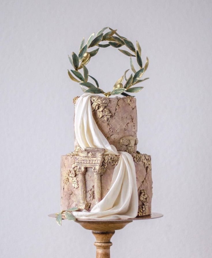 a three tiered cake with white icing and greenery on top, sitting on a wooden stand