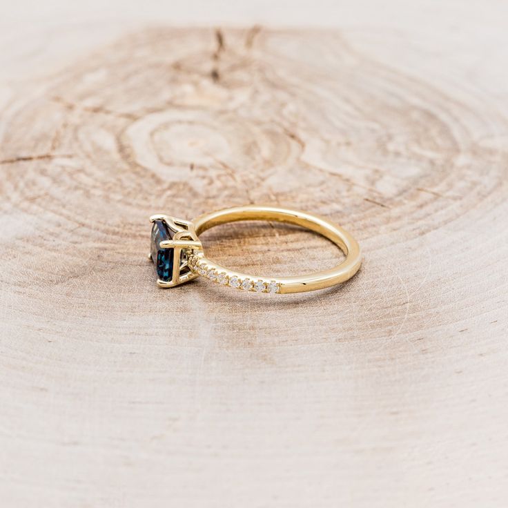 a gold ring with a blue stone and diamond accents on top of a piece of wood