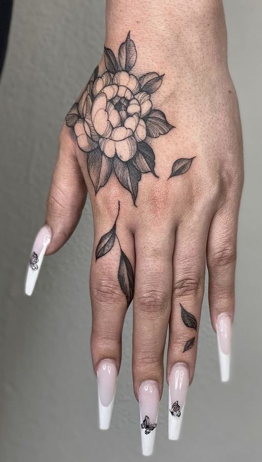 a woman's hand with white and black flowers on her left hand, while the other hand has a flower tattoo on it